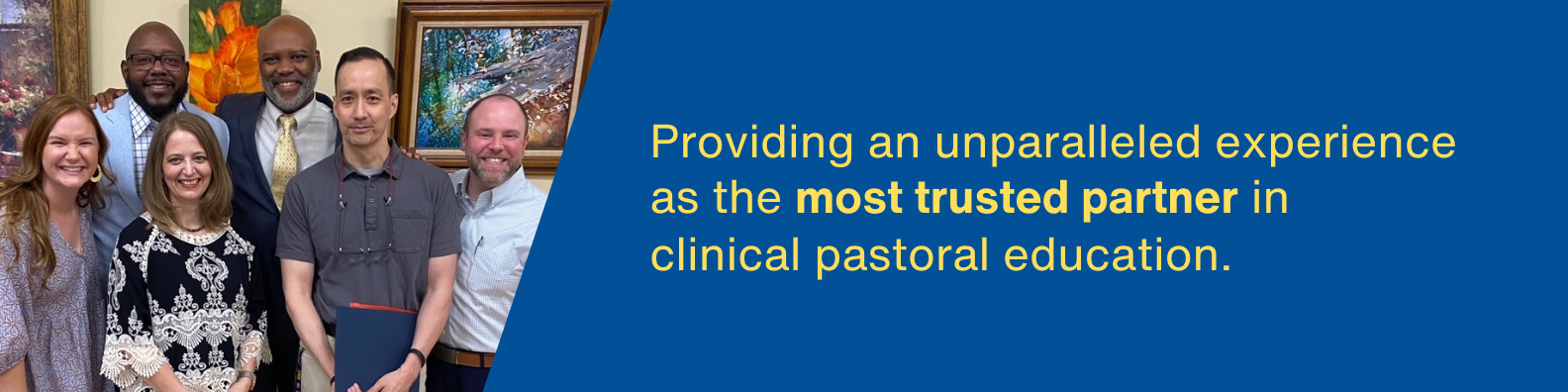 A group of six people, smiling at the camera. They are dressed in business casual clothing, and there are several paintings or scultpures in the background. The colors are vivid - yellow, blues, and orange.